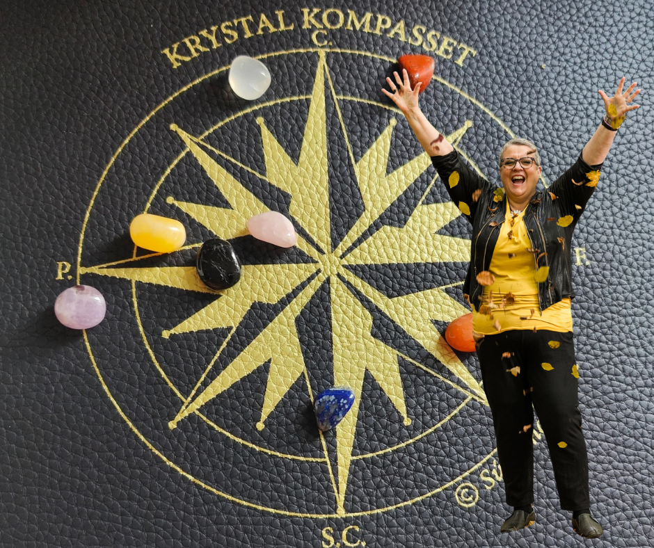 Krystal Kompasset med farvede krystaller på kompasmatte, Súsanna Vígdá står med armene løftet i sejr.